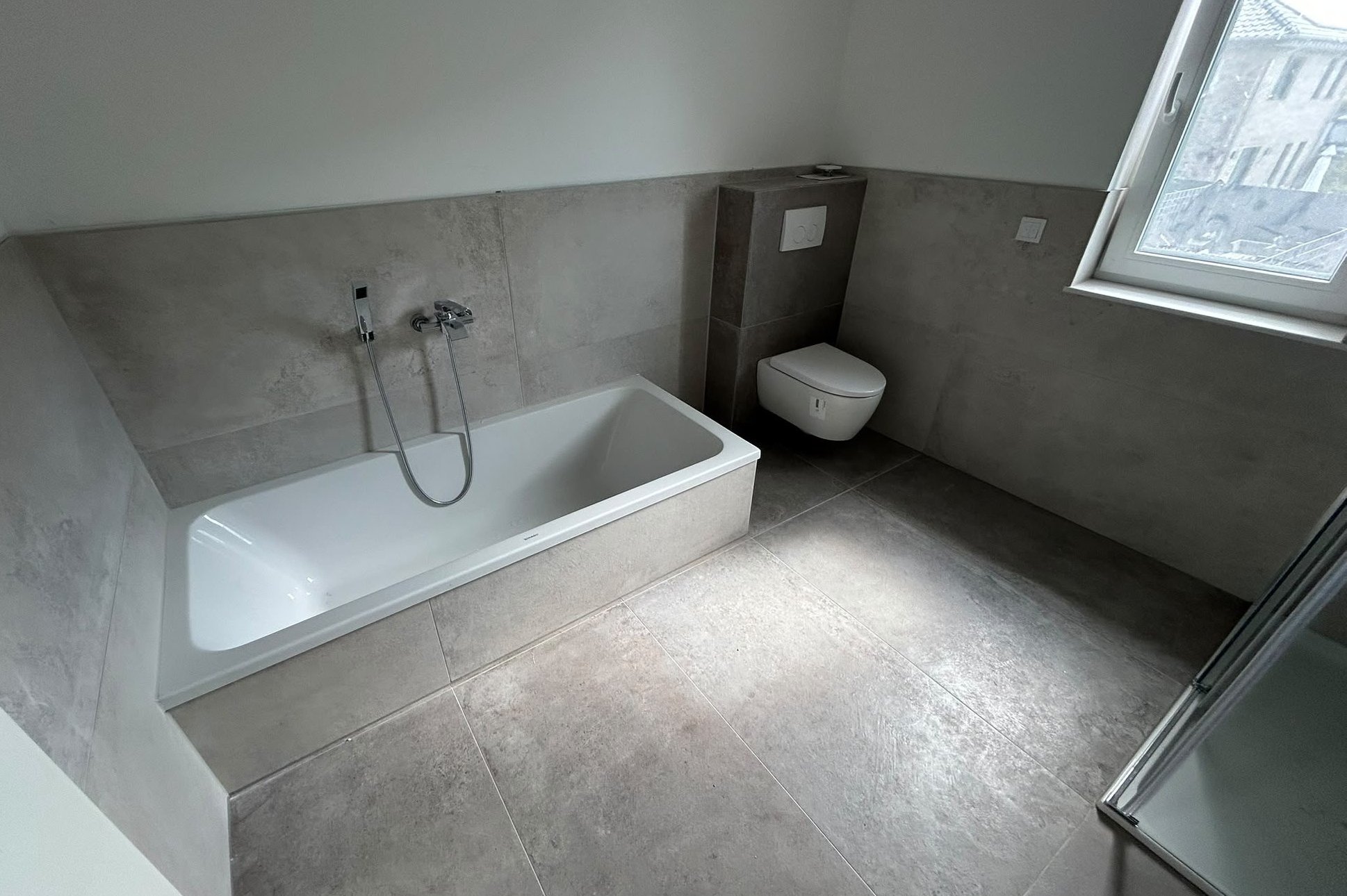 Helles Bad mit großformatigen Fliesen, eingefliester Badewanne und Vorwand-WC
