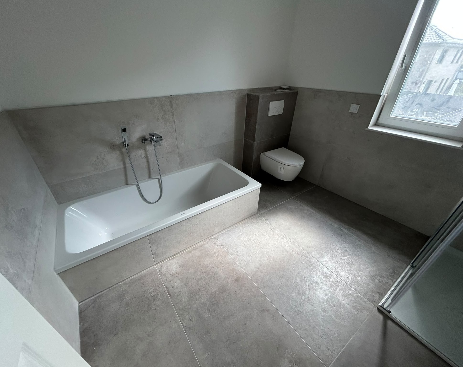 Helles Bad mit großformatigen Fliesen, eingefliester Badewanne und Vorwand-WC