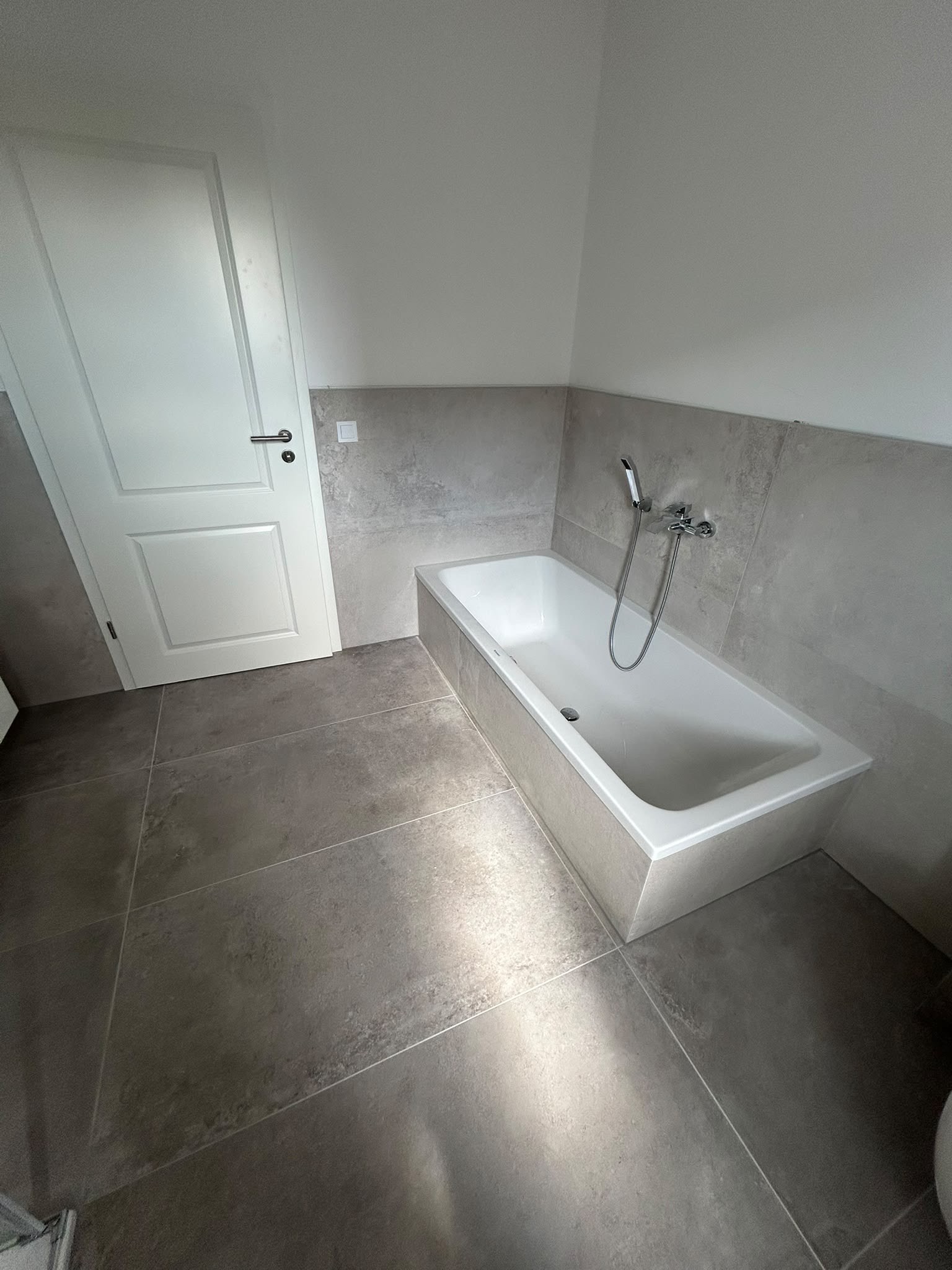 Eingeflieste Badewanne in einem hellen Bad mit großformatigen Fliesen