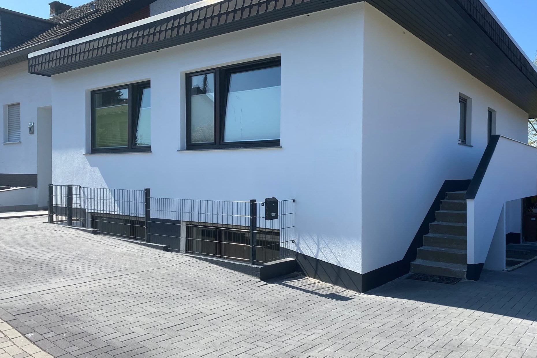 Dasselbe Haus nach der Sanierung: gedämmte Fassade mit hellem Putz, neue Fenster, Stabmattenzaun und neues Pflaster