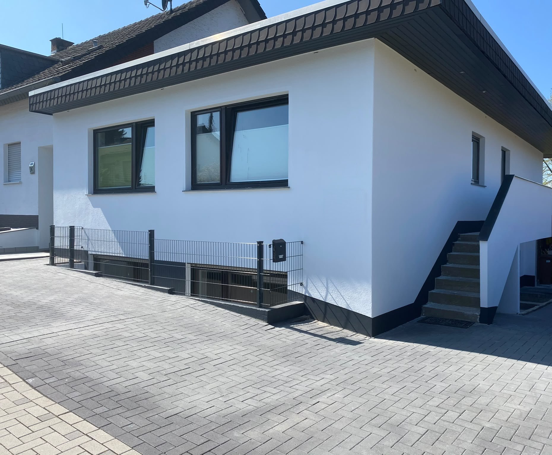 Dasselbe Haus nach der Sanierung: gedämmte Fassade mit hellem Putz, neue Fenster, Stabmattenzaun und neues Pflaster