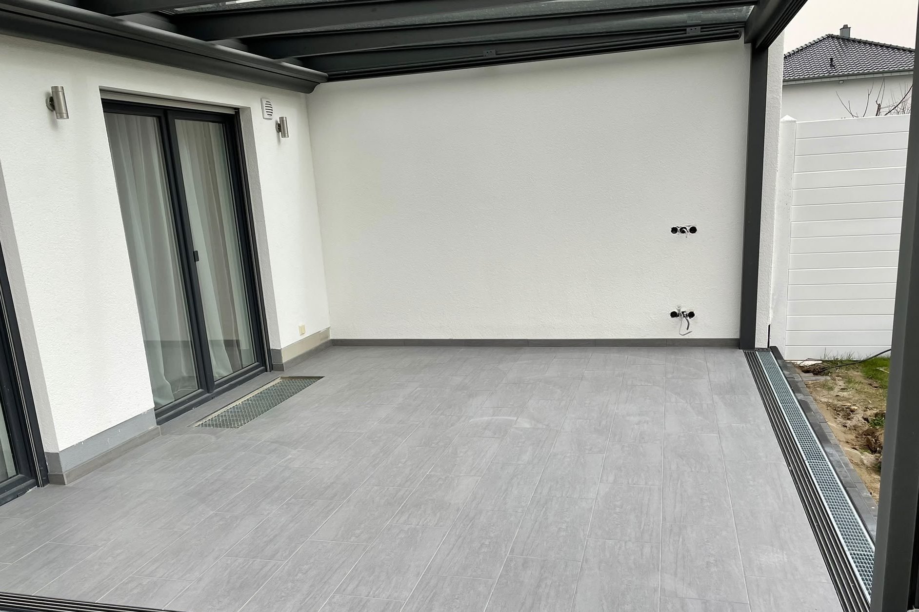 Überdachte Terrasse mit grauem Feinsteinzeugbelag und umlaufender Entwässerungsrinne