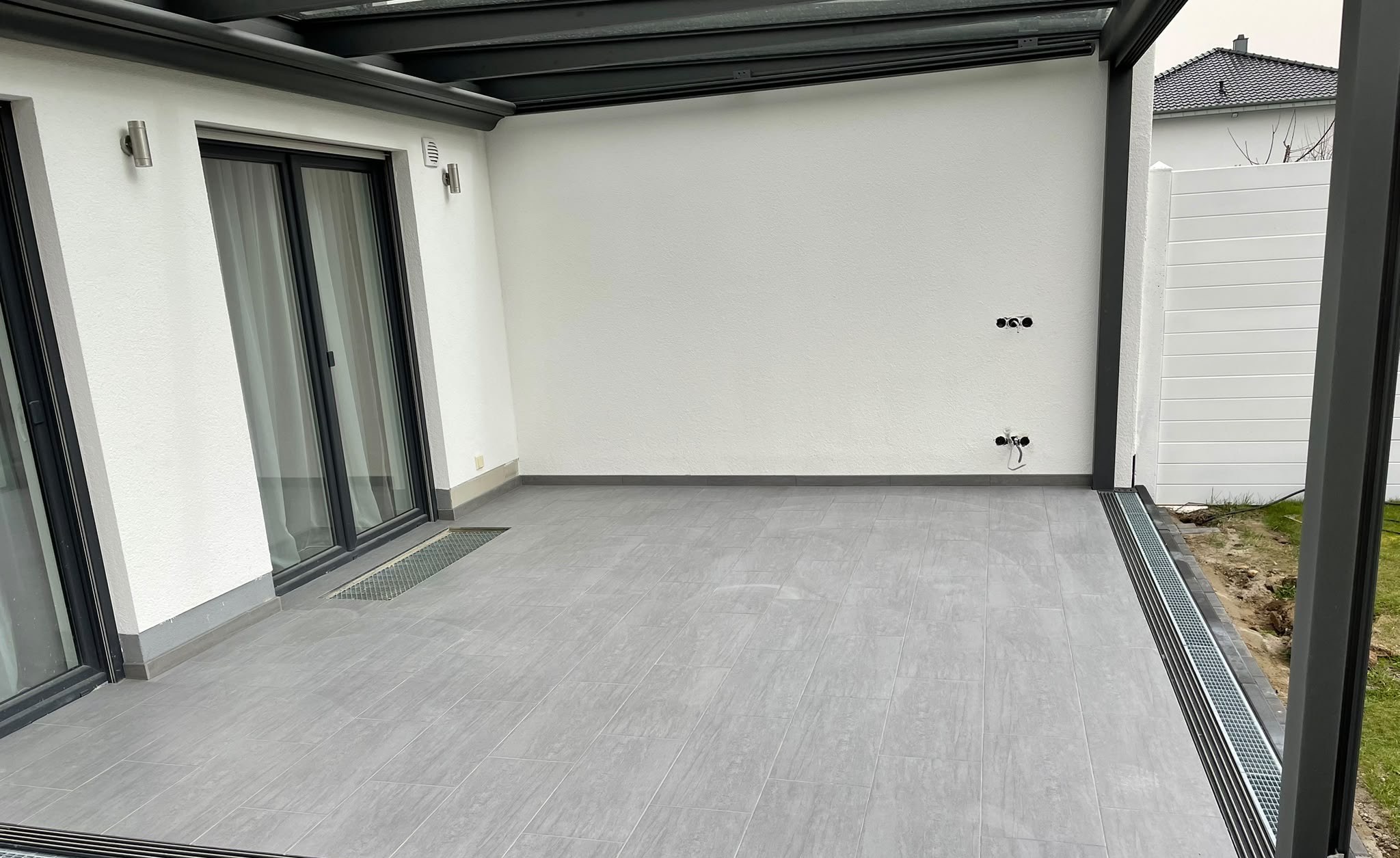 Überdachte Terrasse mit grauem Feinsteinzeugbelag und umlaufender Entwässerungsrinne